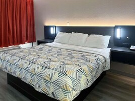 Quarto de hotel com uma cama, duas mesas de cabeceira, uma cortina vermelha e um cobreleite estampado.