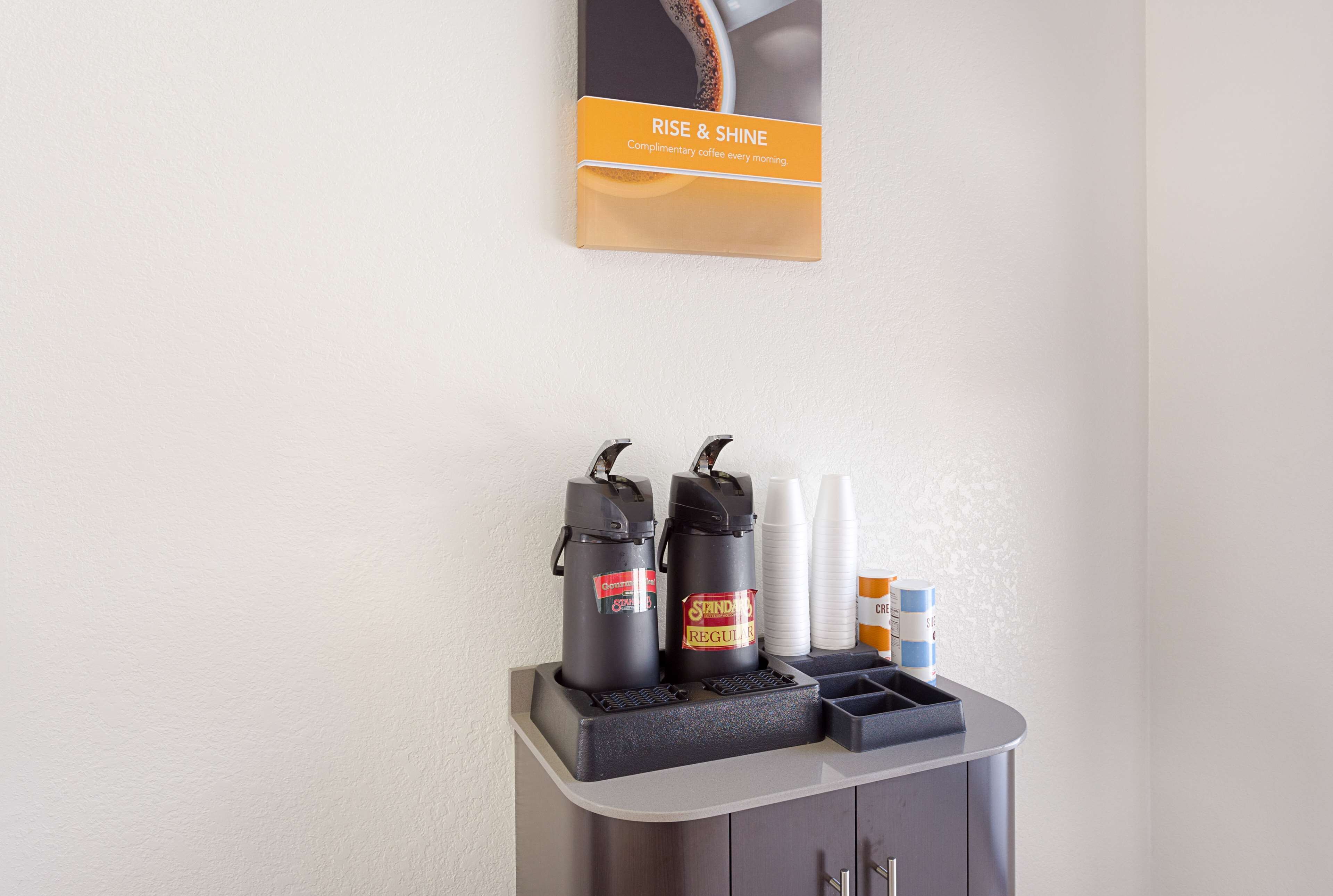 A coffee station with two coffee dispensers, disposable cups, and a creamer dispenser.