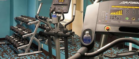 A gym with various exercise equipment, including treadmills and dumbbells, and a water bottle on the machine.