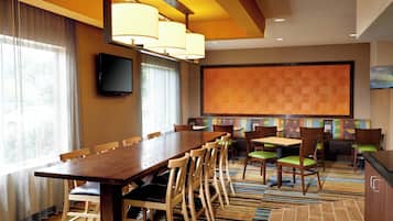 A conference room with a long table, multiple chairs, a flat-screen TV, and a large screen on the wall.