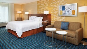 A hotel room with a large bed, a sofa, two small tables, and a wall art piece. - Fairfield Inn By Marriott Port Huron (Port Huron)
