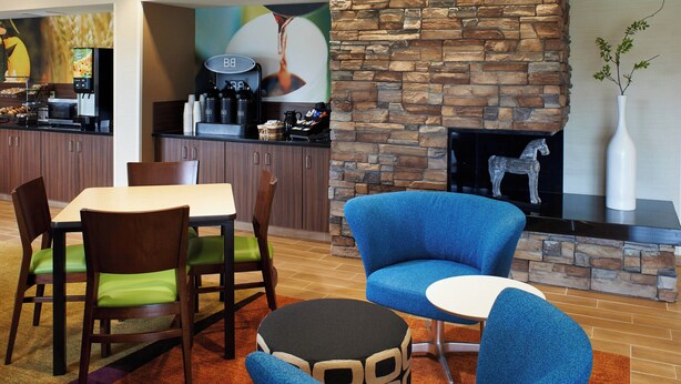 A modern dining area with a stone fireplace, a coffee station, and comfortable seating. - Fairfield Inn By Marriott Port Huron (Port Huron)