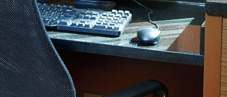 Ein Computermonitor zeigt die Hotelwebsite, daneben eine Tastatur, eine Maus und ein Stuhl vor einem Holzbüro mit einem Schild, das den Namen und die Adresse des Hotels angibt.
