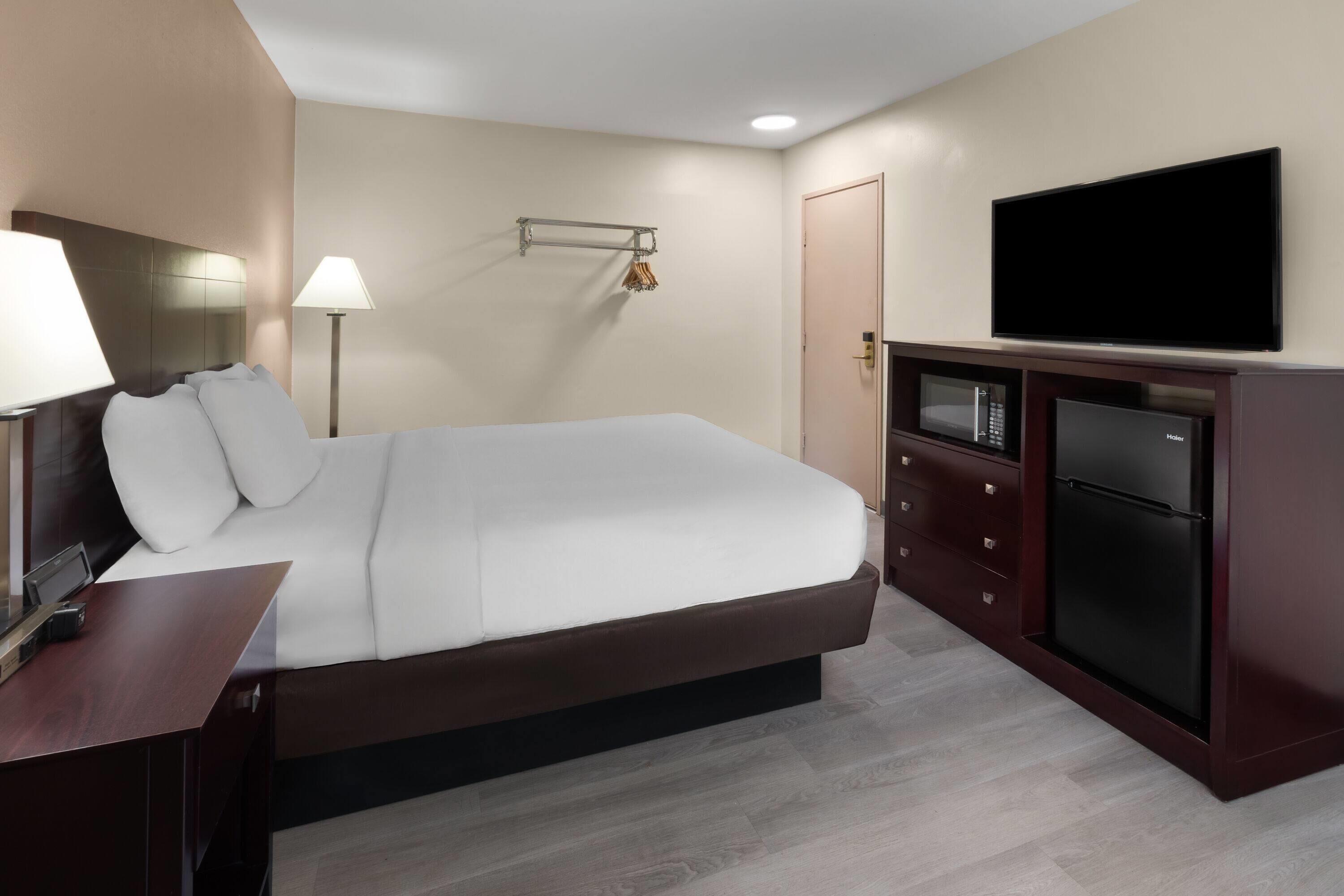 Una camera d'albergo con un letto grande, una televisione a schermo piatto, un minibar e una scrivania con una lampada.