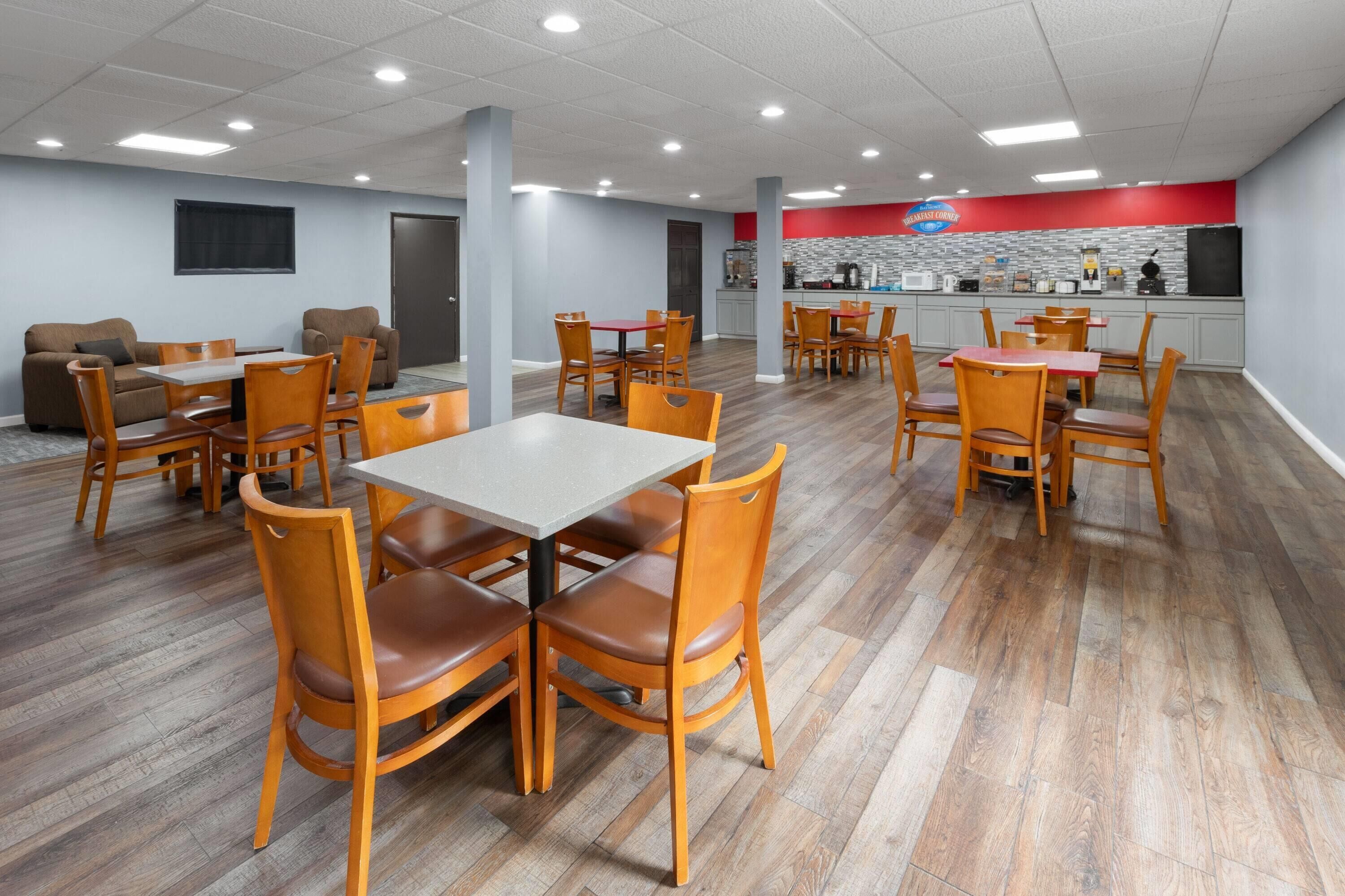 Un grand espace de salle à manger avec des tables et des chaises en bois, un comptoir de cuisine et un mur d’accent rouge.