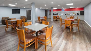 Un comedor amplio con mesas y sillas de madera, una encimera de cocina y una pared roja decorativa.