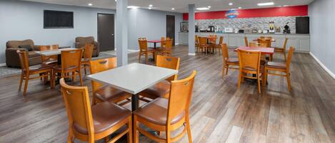 Un grand espace de salle à manger avec des tables et des chaises en bois, un comptoir de cuisine et un mur d’accent rouge.