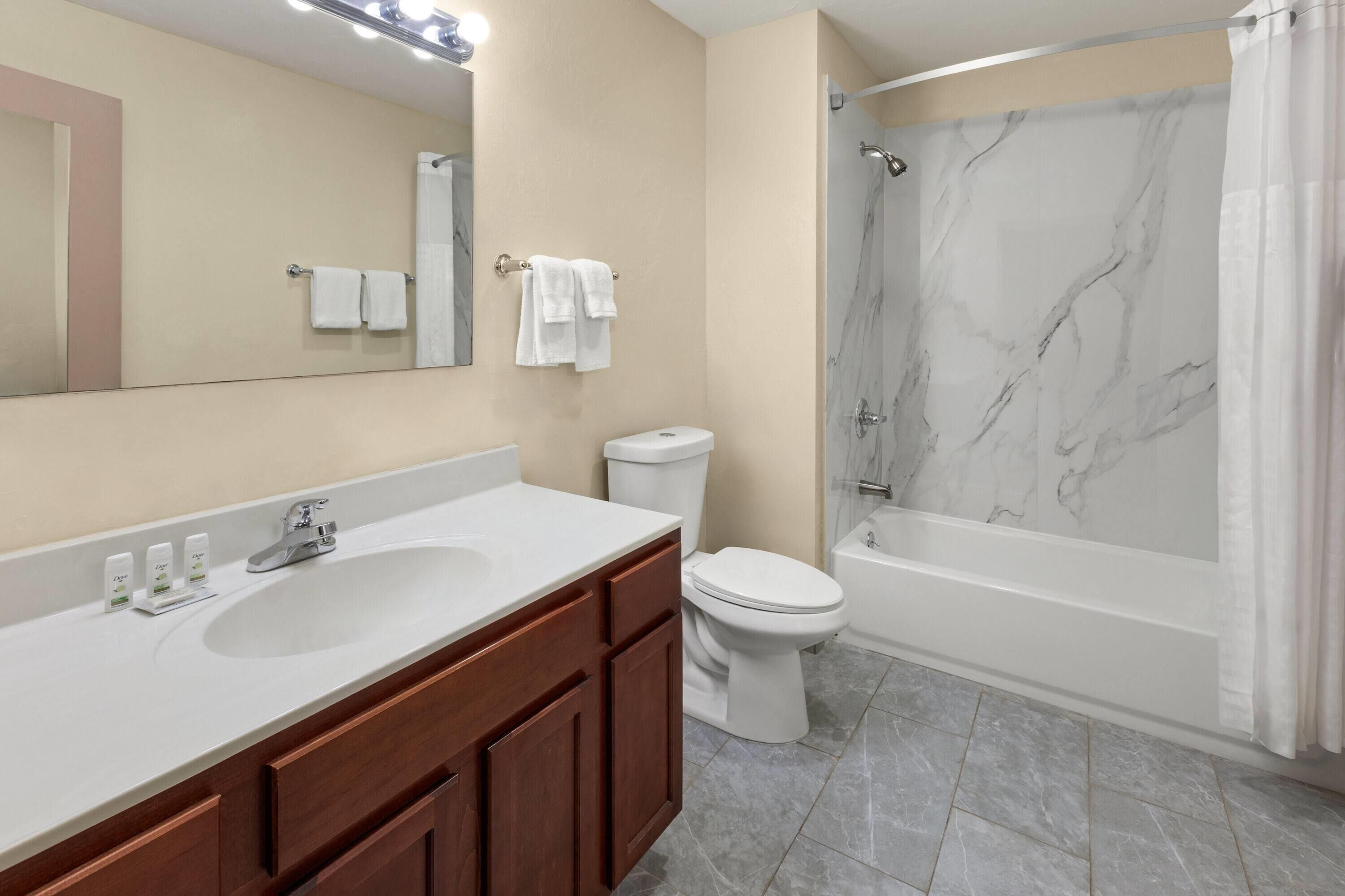 A bathroom with a marble shower wall, a white sink, and a toilet.