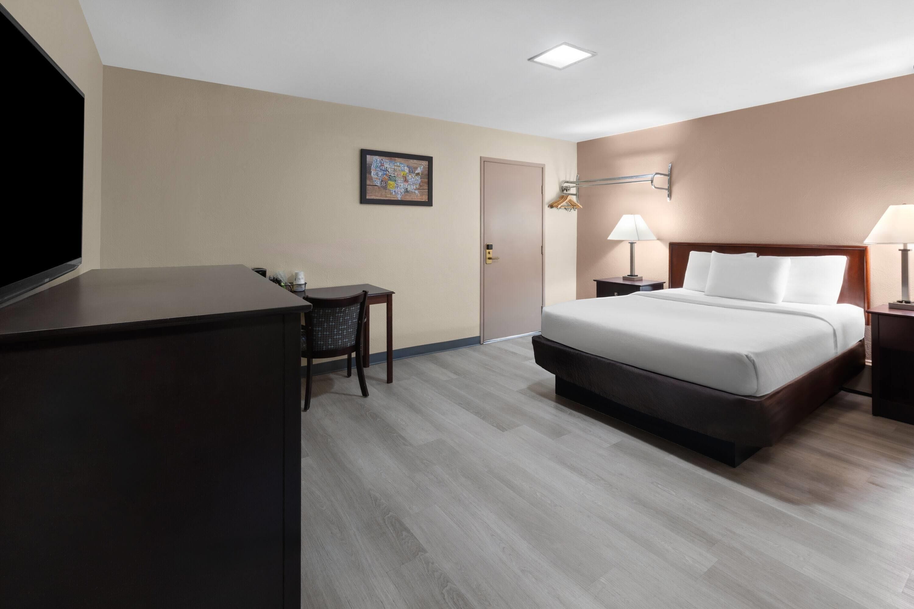 Una habitación de hotel con cama, mesitas de noche, un escritorio, una silla, televisión y puerta.