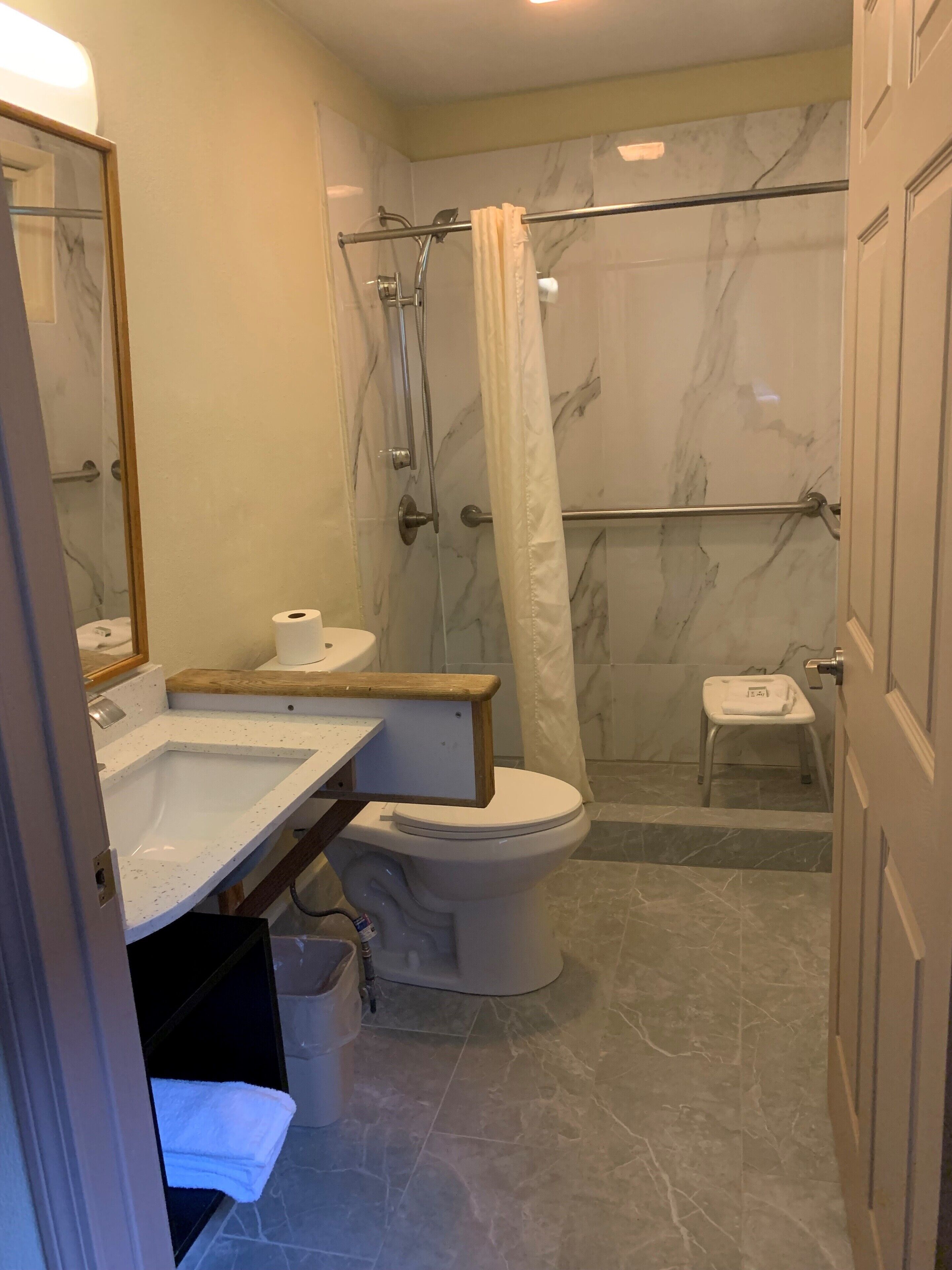 A bathroom with a marble shower, a toilet, a sink, and a mirror.