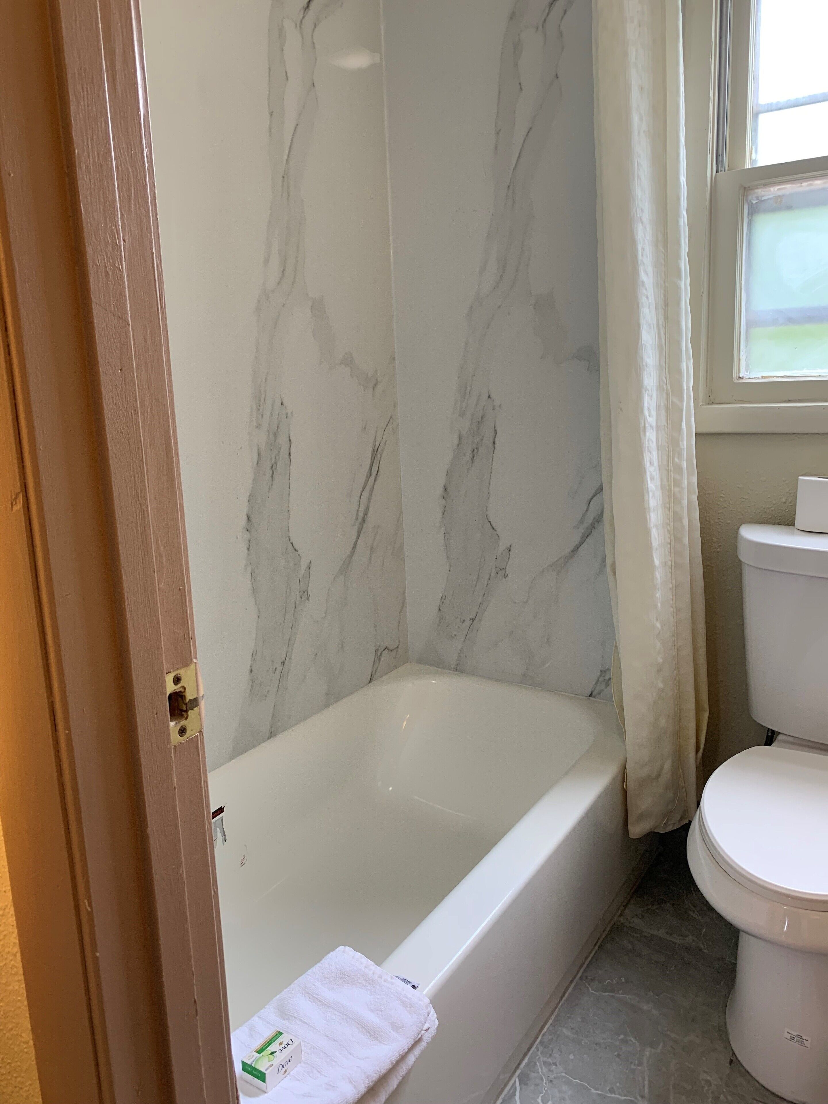 A bathroom with a marble wall, a bathtub, and a toilet.