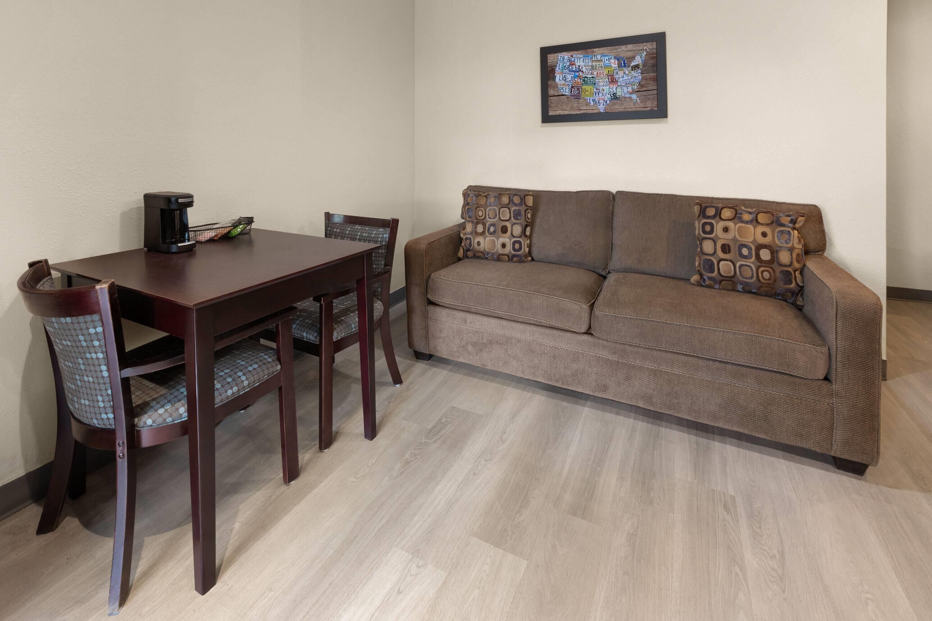 Una sala de estar amoblada con una mesa de comedor de madera, dos sillas, un sofá con cojines estampados y un mapa enmarcado en la pared.