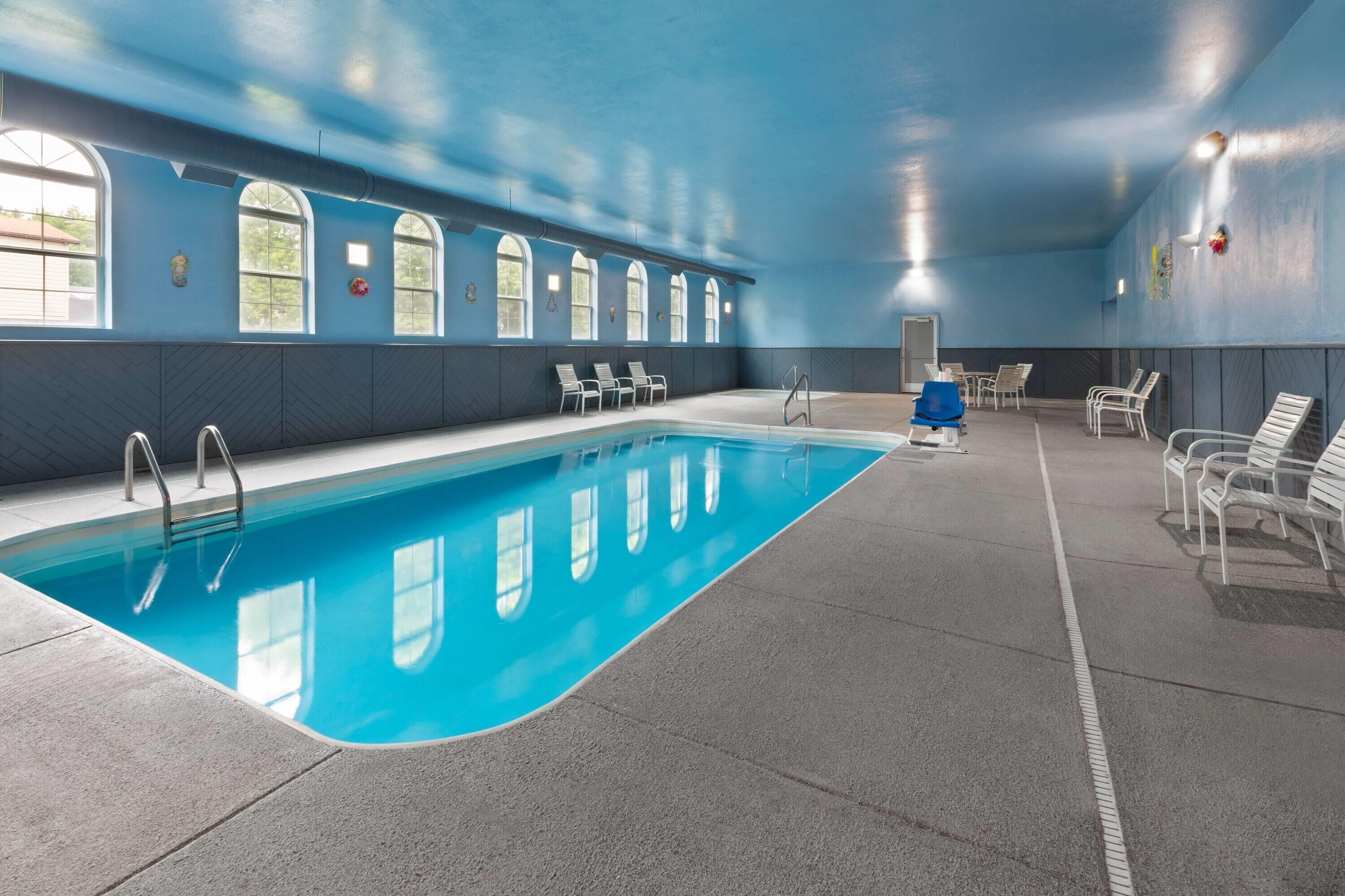 En indendørs swimmingpool med klart, blåt vand, omgivet af liggestole og et blåt loft.