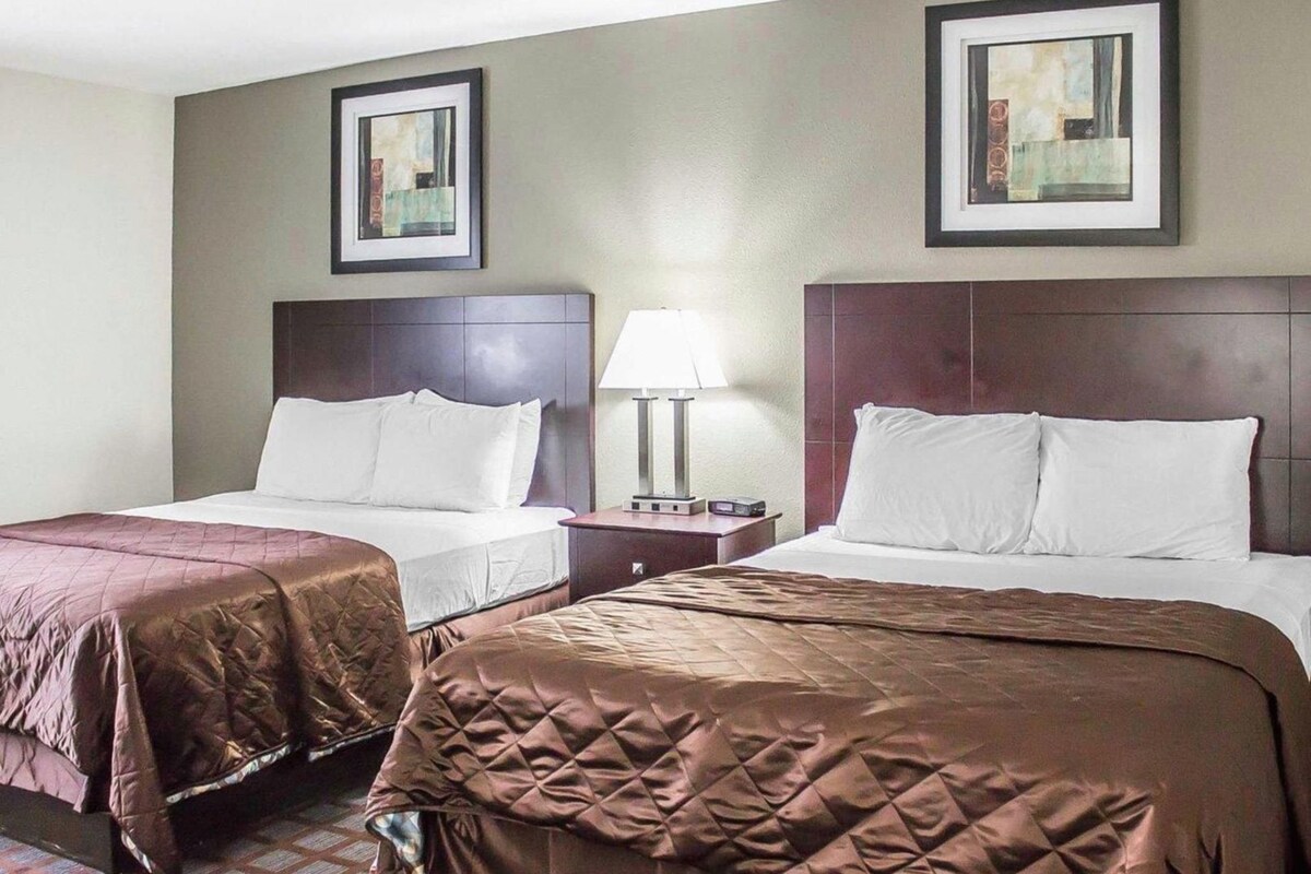 A hotel room with two beds, a nightstand with a lamp, and two framed pictures on the wall.