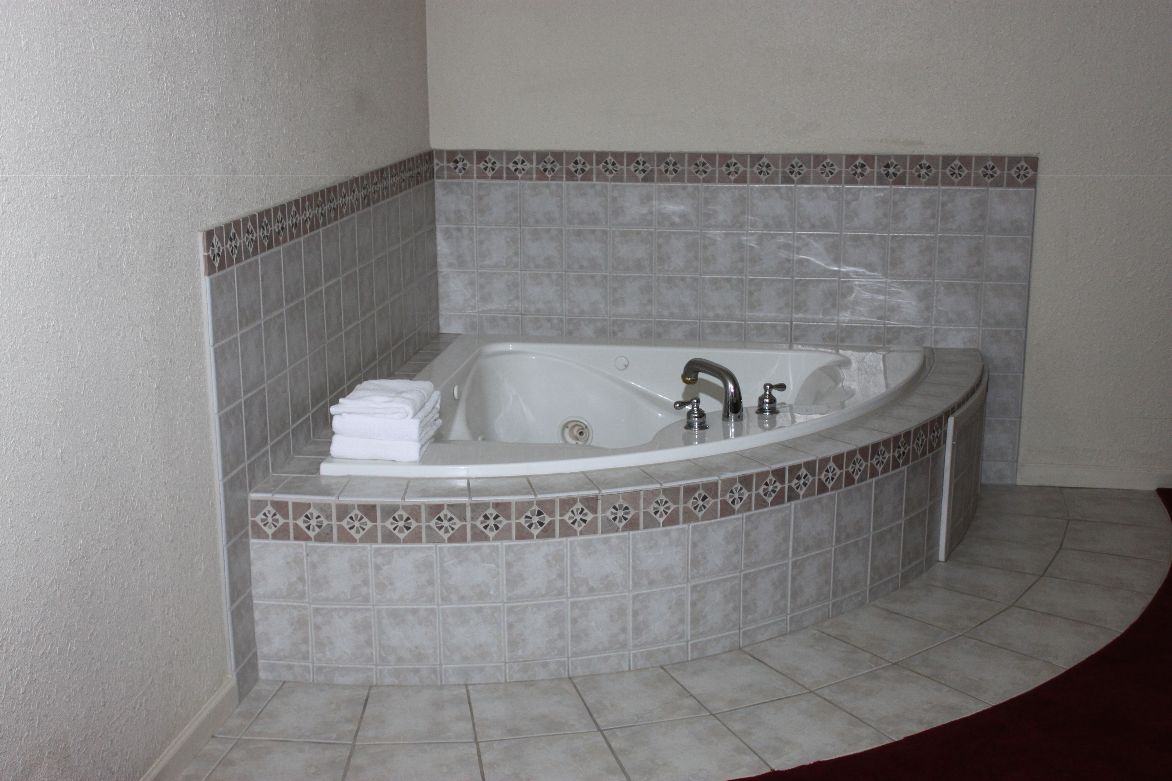 A corner bathtub with a curved design, a built-in shower, and a decorative tile border.