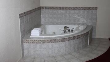A corner bathtub with a curved design, a built-in shower, and a decorative tile border.
