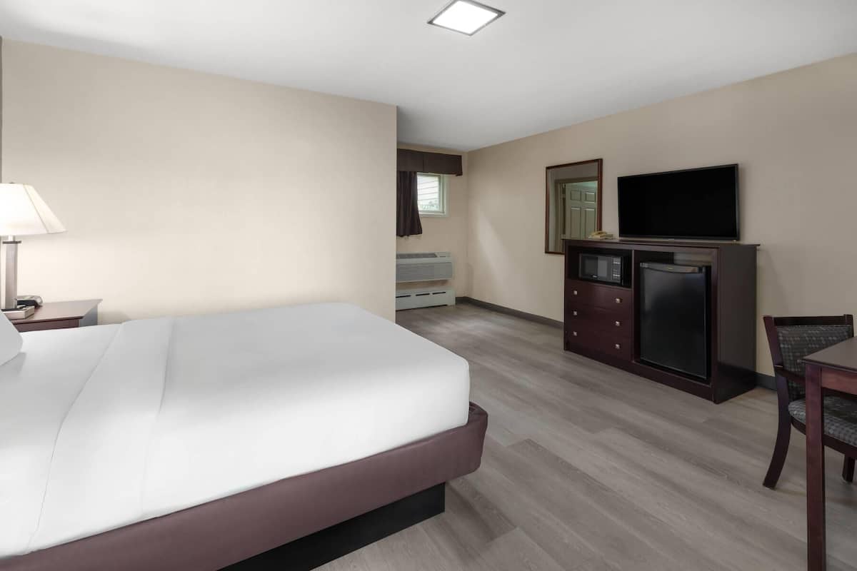 A hotel room with a bed, a desk, a television, a microwave, and a dresser.