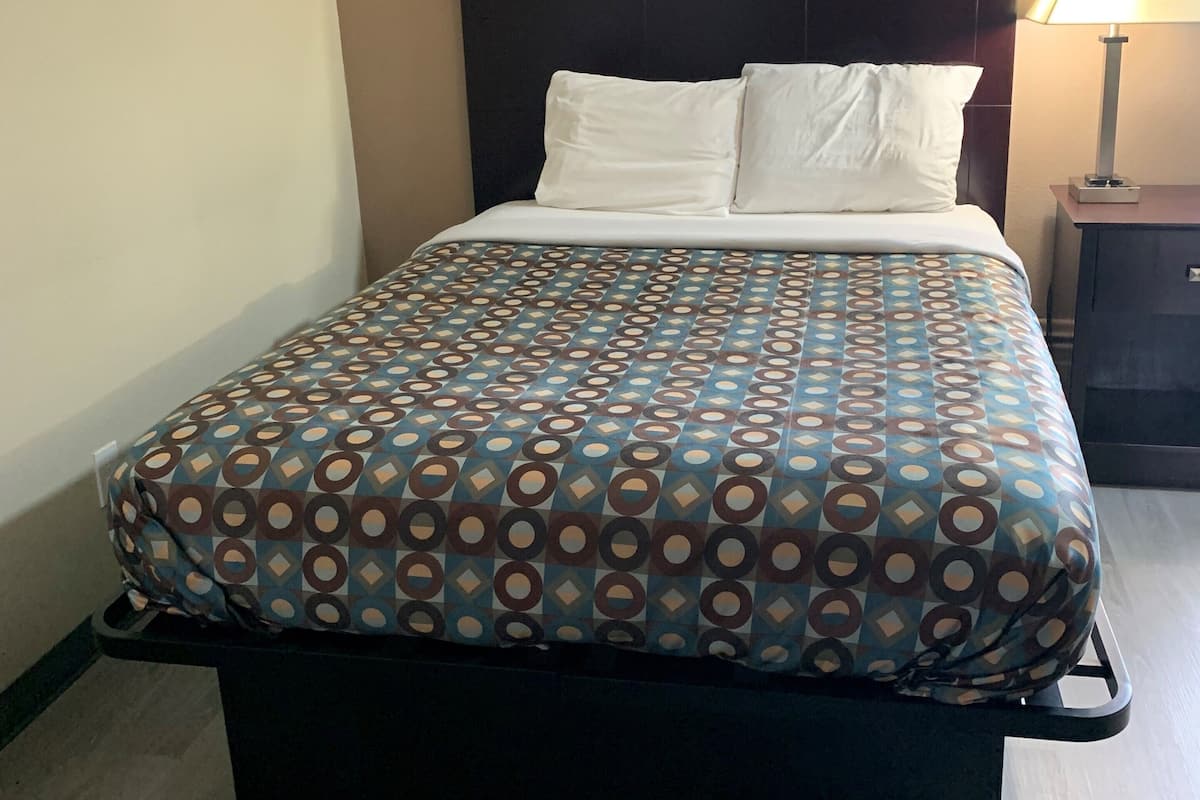 A neatly made bed with a patterned bedspread, a dark headboard, and a bedside table with a lamp.