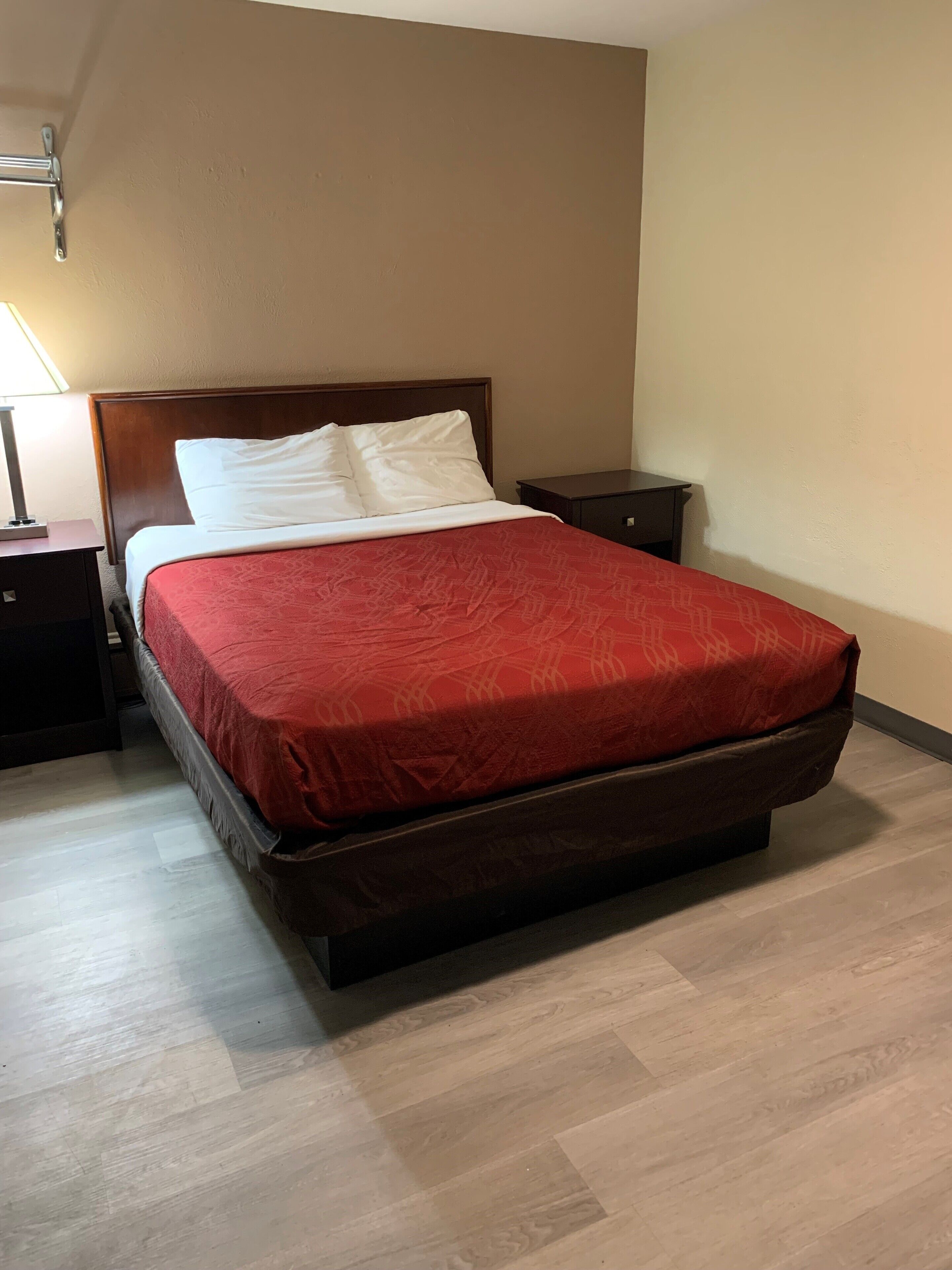 A hotel room with a large bed, a nightstand, a lamp, and a wooden floor.