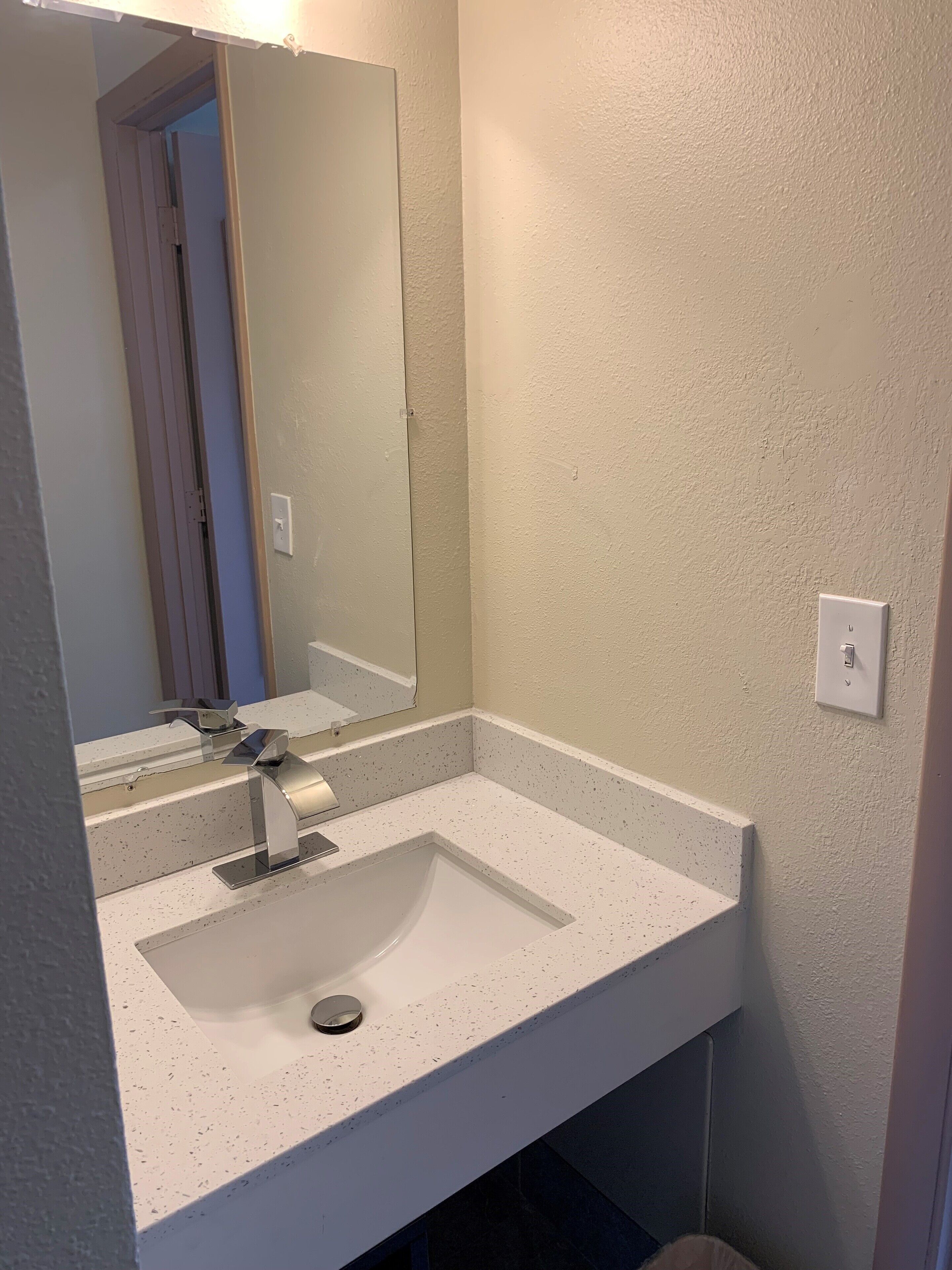 A bathroom with a white sink, a mirror, and a light switch on the wall.