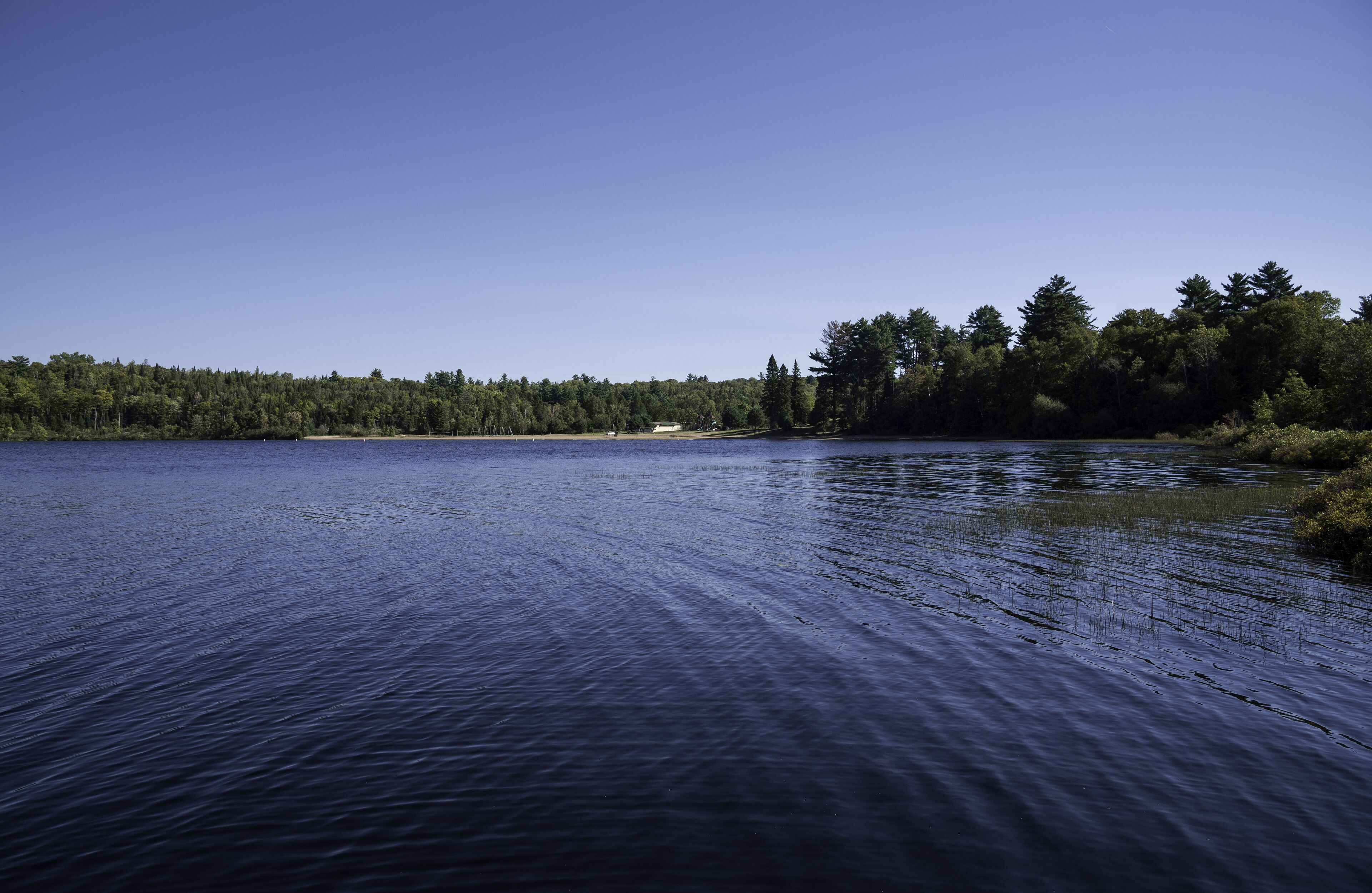 A calm lake with a forested shoreline and a small building in the distance.