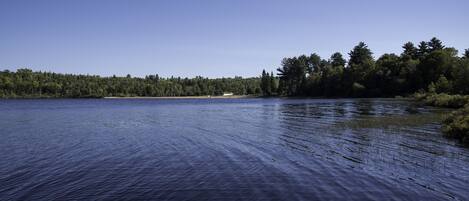 A calm lake with a forested shoreline and a small building in the distance.