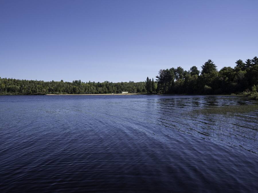A calm lake with a forested shoreline and a small building in the distance.