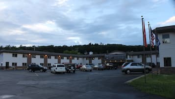 A parking lot with several cars, a building with multiple windows, and flags on poles.