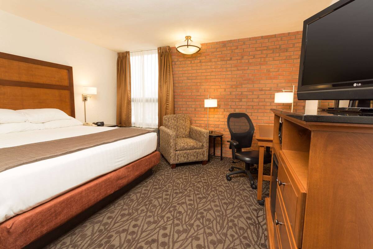 A hotel room with a large bed, a wooden desk, a television, and a chair.