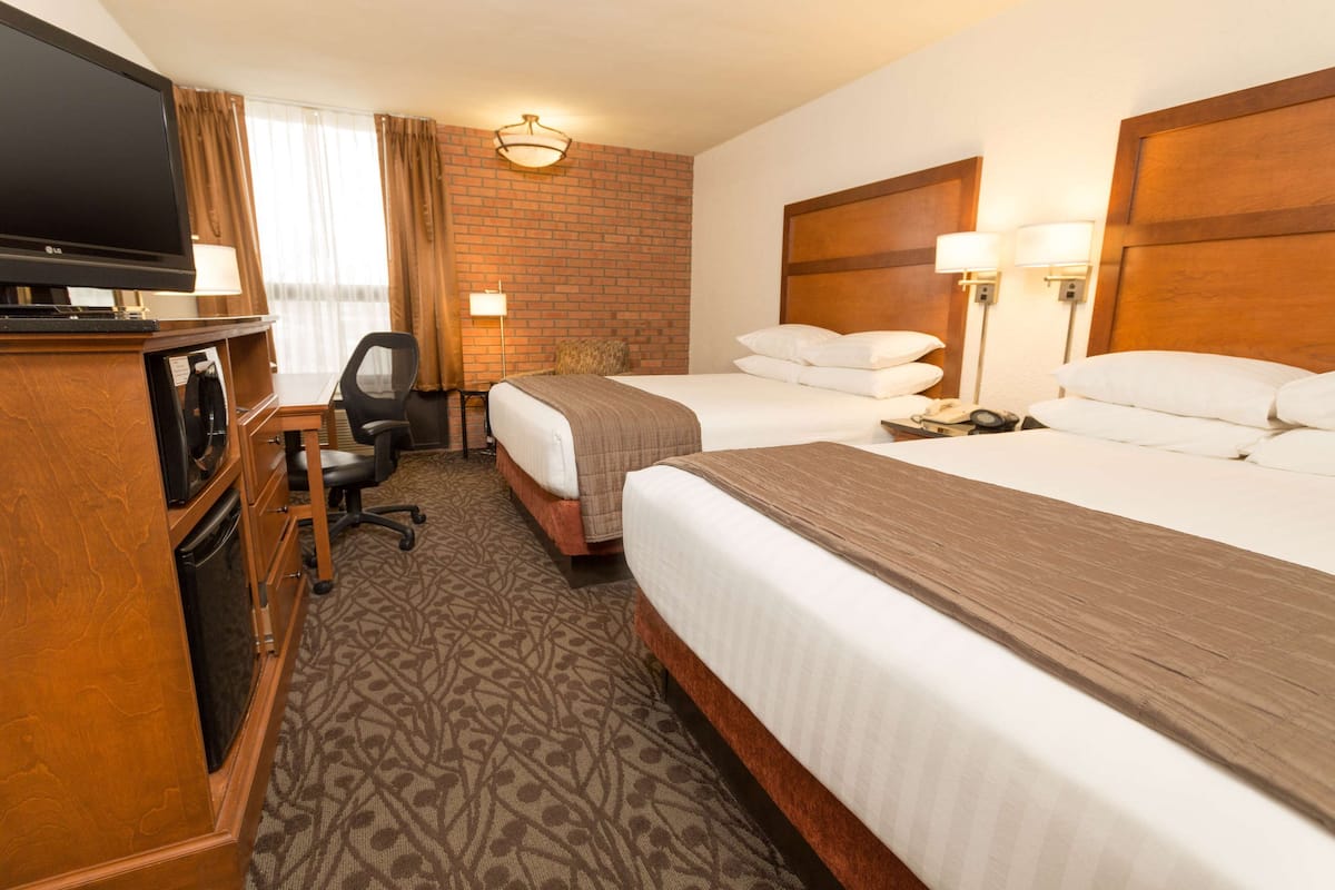 A hotel room with two beds, a TV, a desk with a chair, and a brick wall.