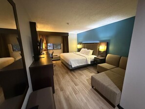 Quarto de hotel com cama, escrivaninha, cadeira e sofá.