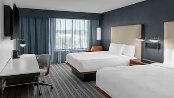 A hotel room with two beds, a desk, a chair, and a TV.
