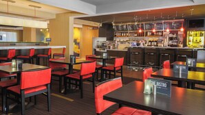 Un restaurante con sillas y mesas tapizadas en rojo, una zona de bar con un menú y una barra con caja registradora.