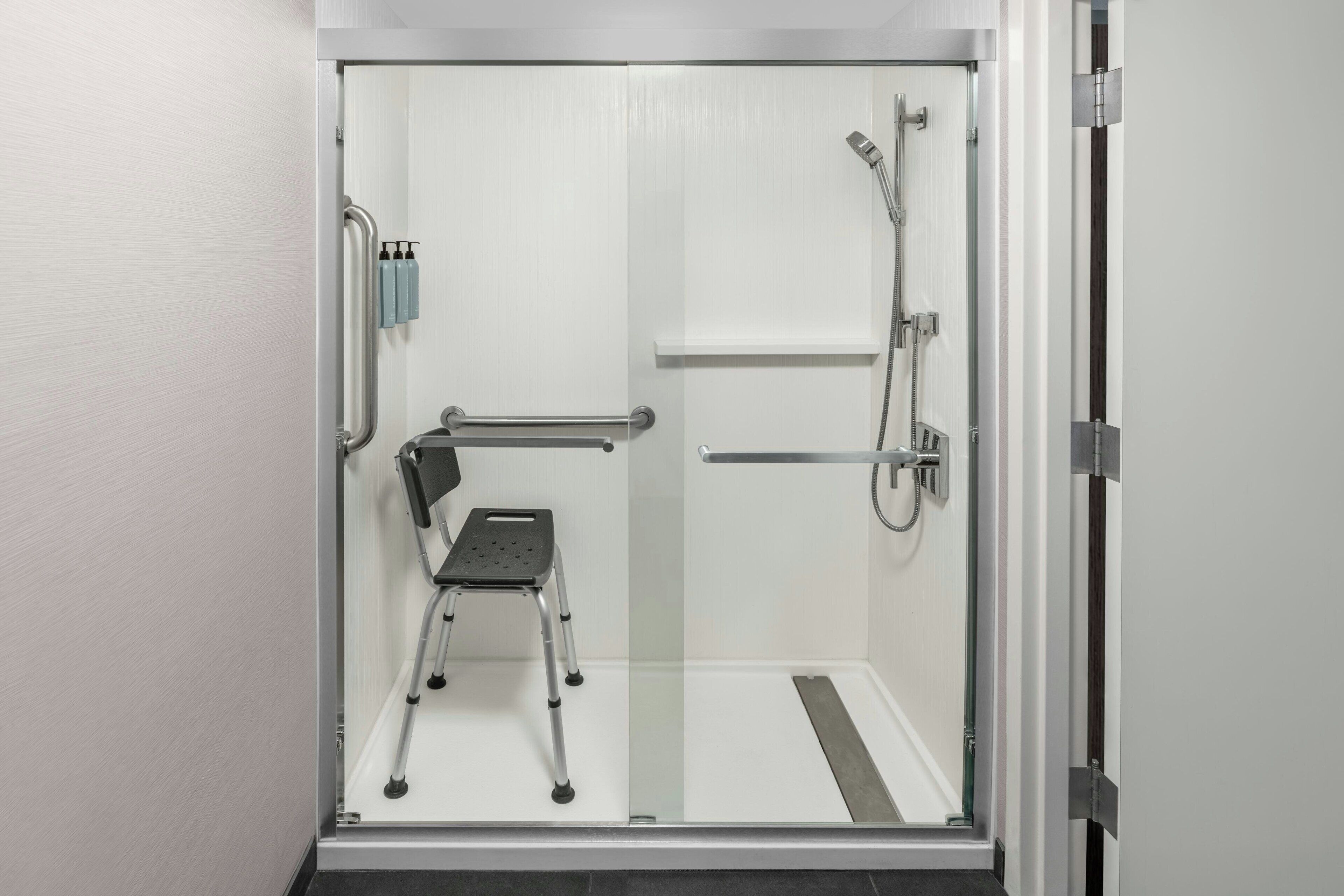 A modern shower stall with a glass door, a handheld showerhead, a handheld shower attachment, and a step stool.