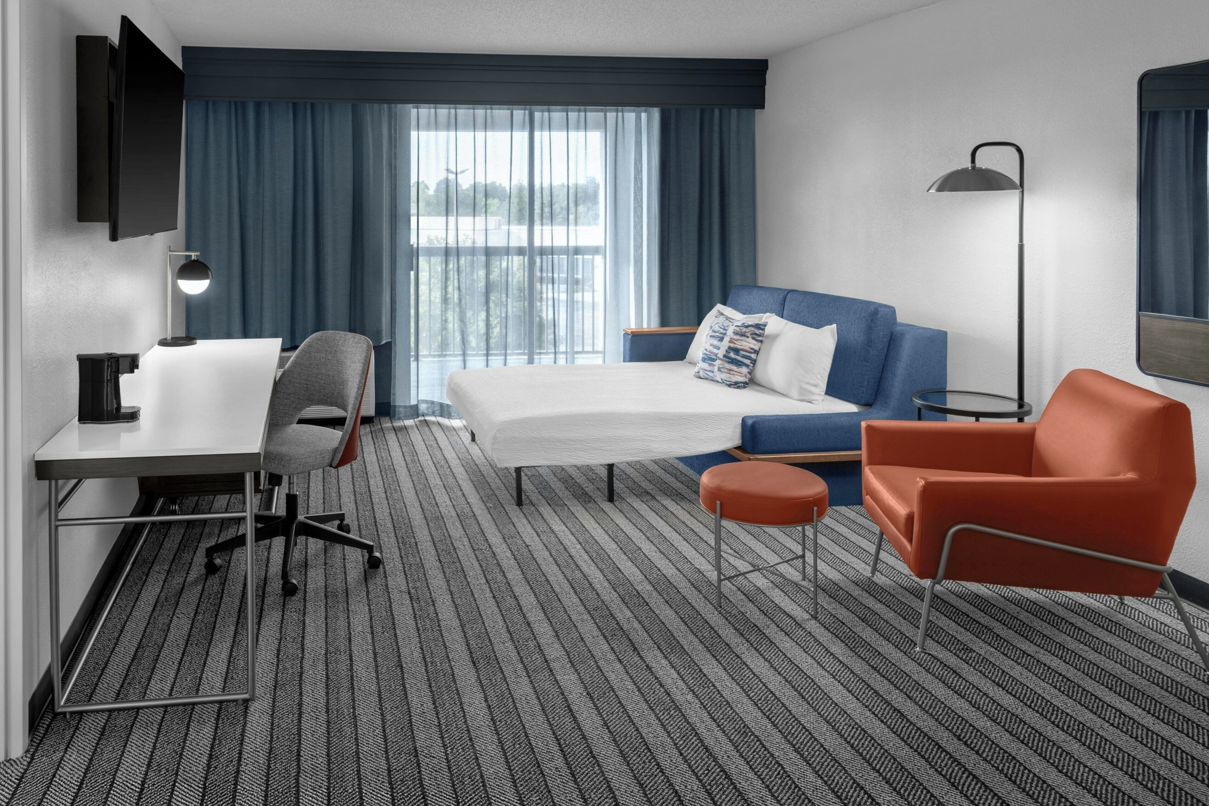 A hotel room with a bed, a desk, a chair, a sofa, and a small table.