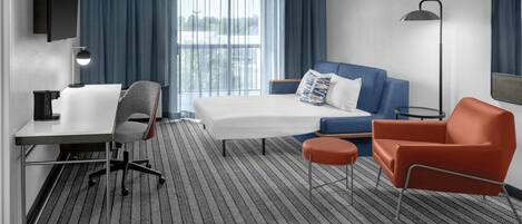 A hotel room with a bed, a desk, a chair, a sofa, and a small table.