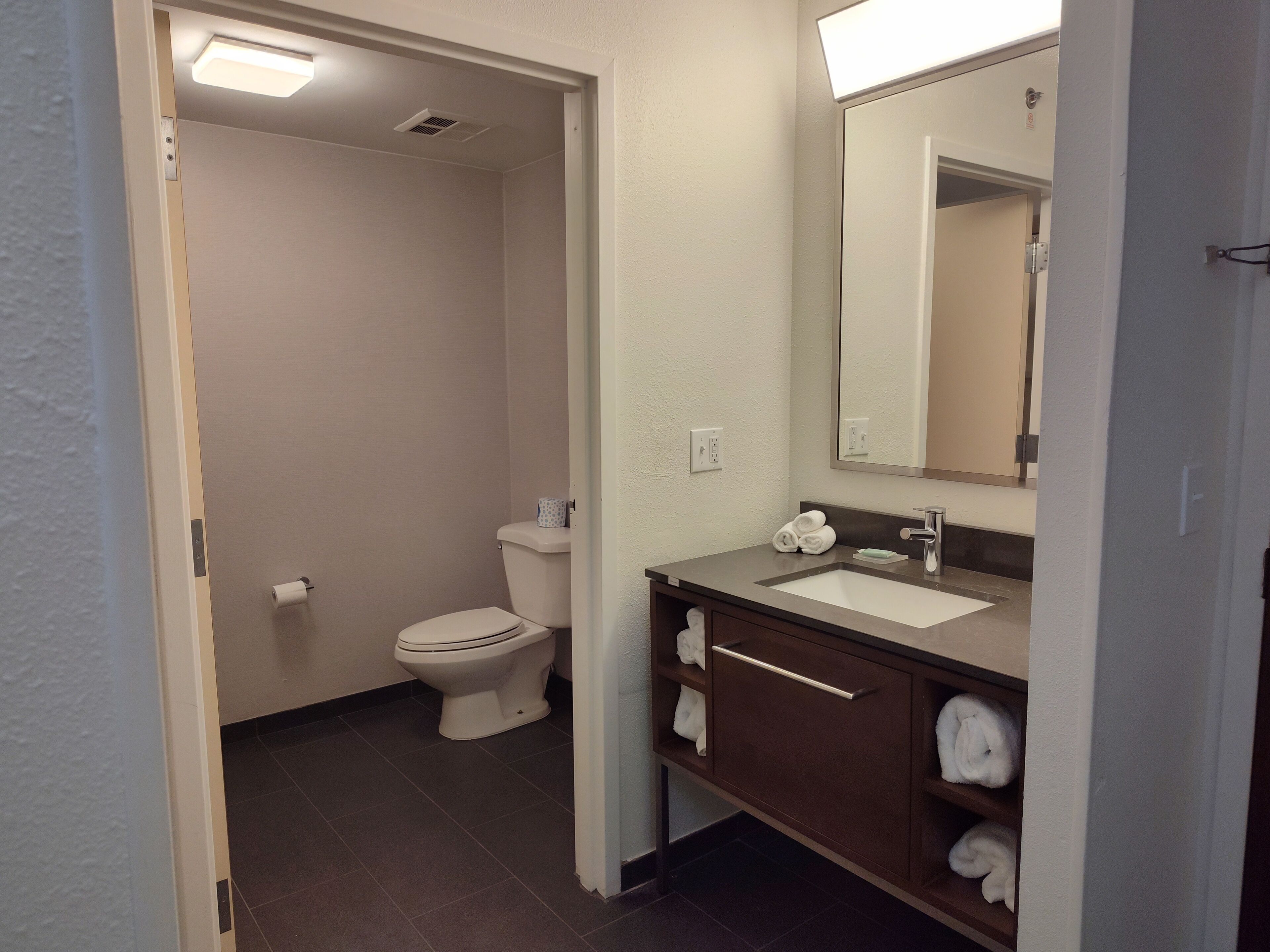 A bathroom with a toilet, sink, mirror, and towel storage.