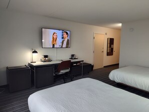 A hotel room with a bed, a desk with a chair, a television, and a door. - Courtyard Flint by Marriott (Flint)