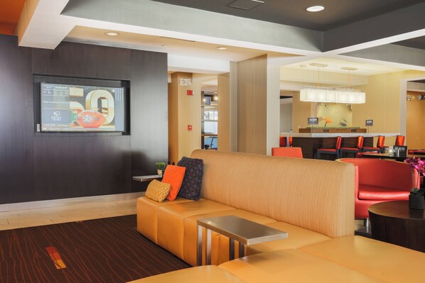 A modern lobby with a seating area, a reception desk, and a dining area. - Courtyard Flint by Marriott (Flint)