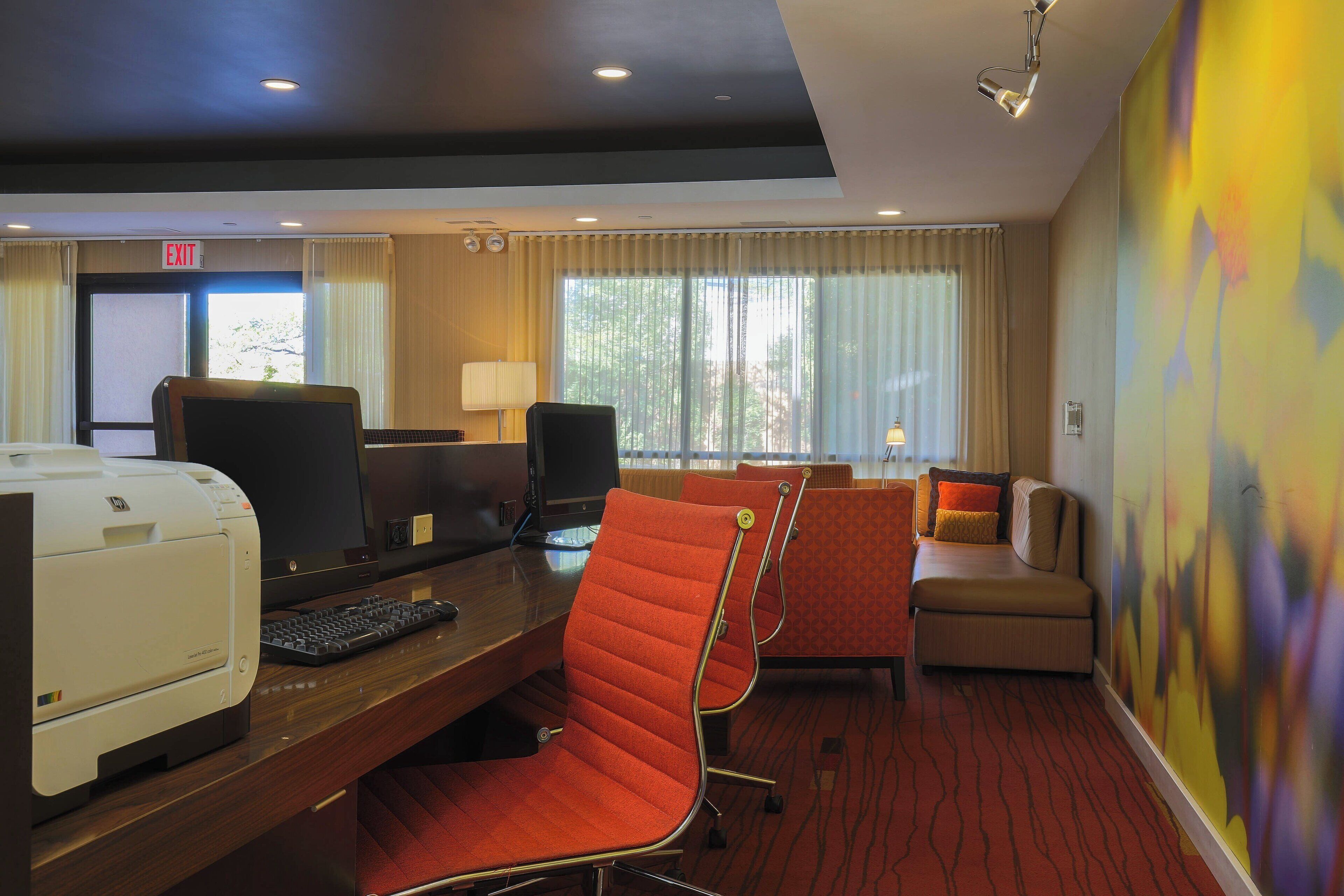 A hotel room with a desk, computers, a printer, and a sofa.