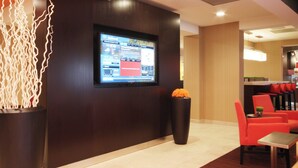 Un vestíbulo moderno con una gran televisión de pantalla plana montada en la pared, un mostrador de recepción y una zona de estar con sillas rojas.
