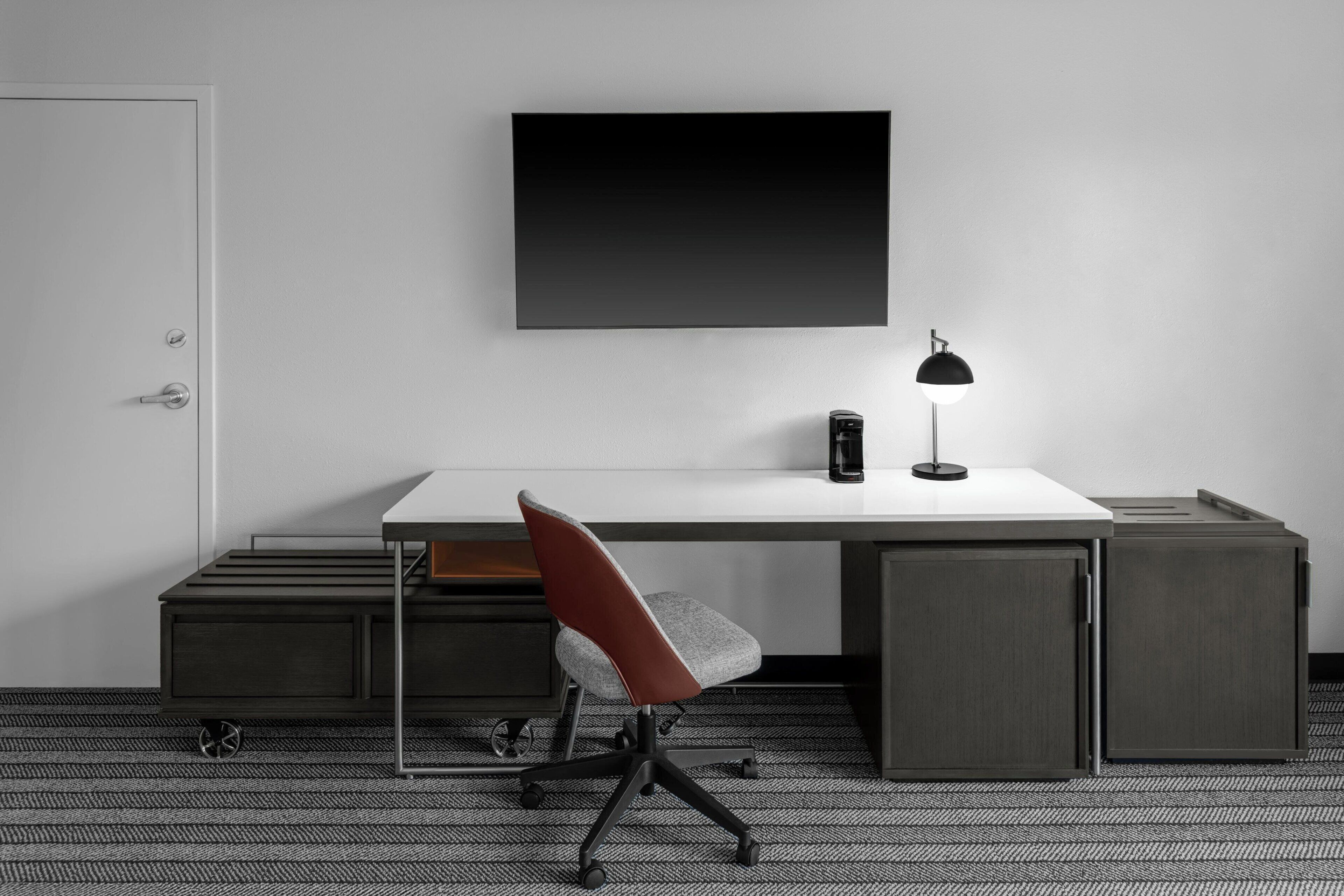 A modern office desk with a chair, a lamp, and a monitor on the wall.