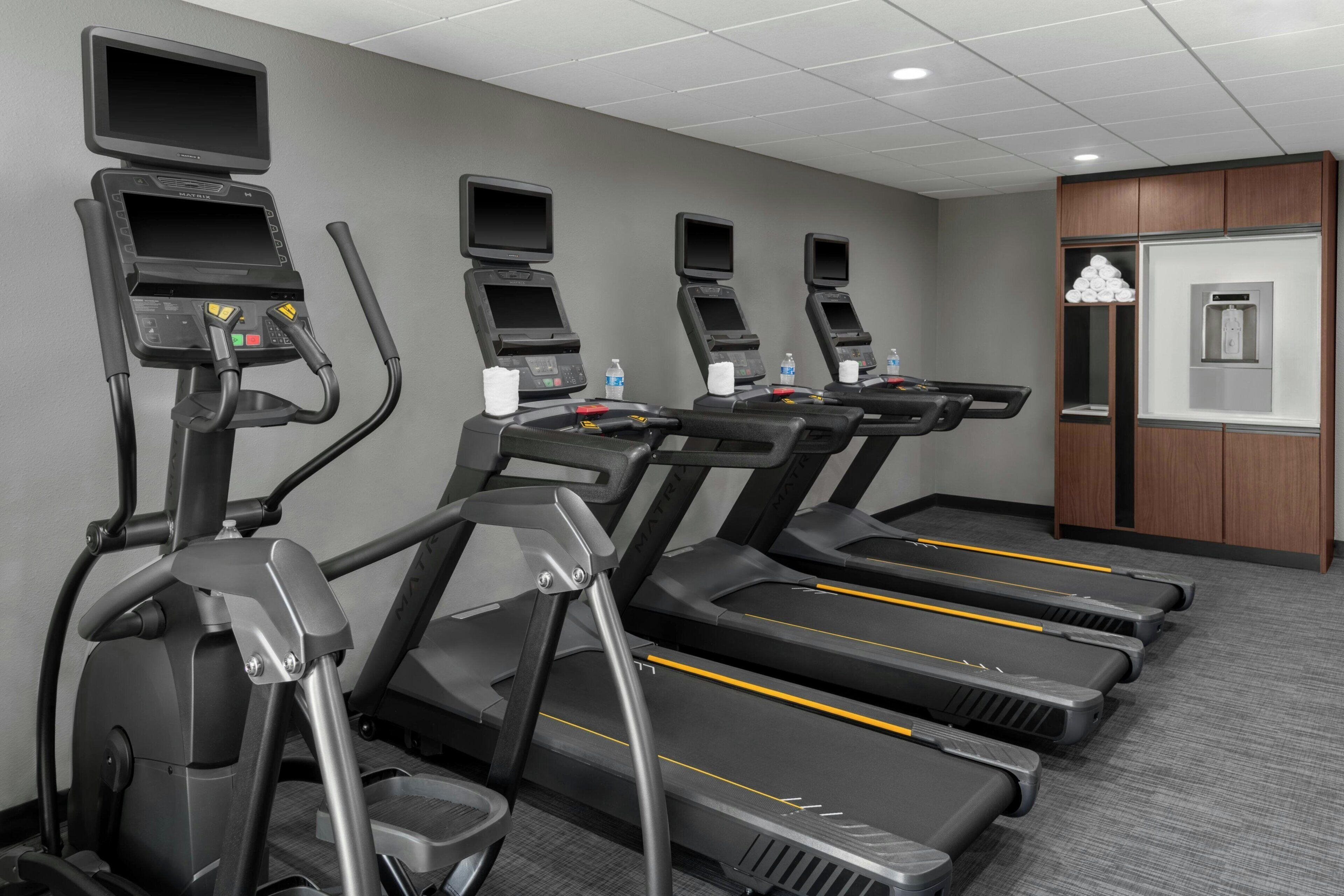 Varias cintas de correr en el gimnasio de un hotel, con paneles de control y botellas de agua en cada una.