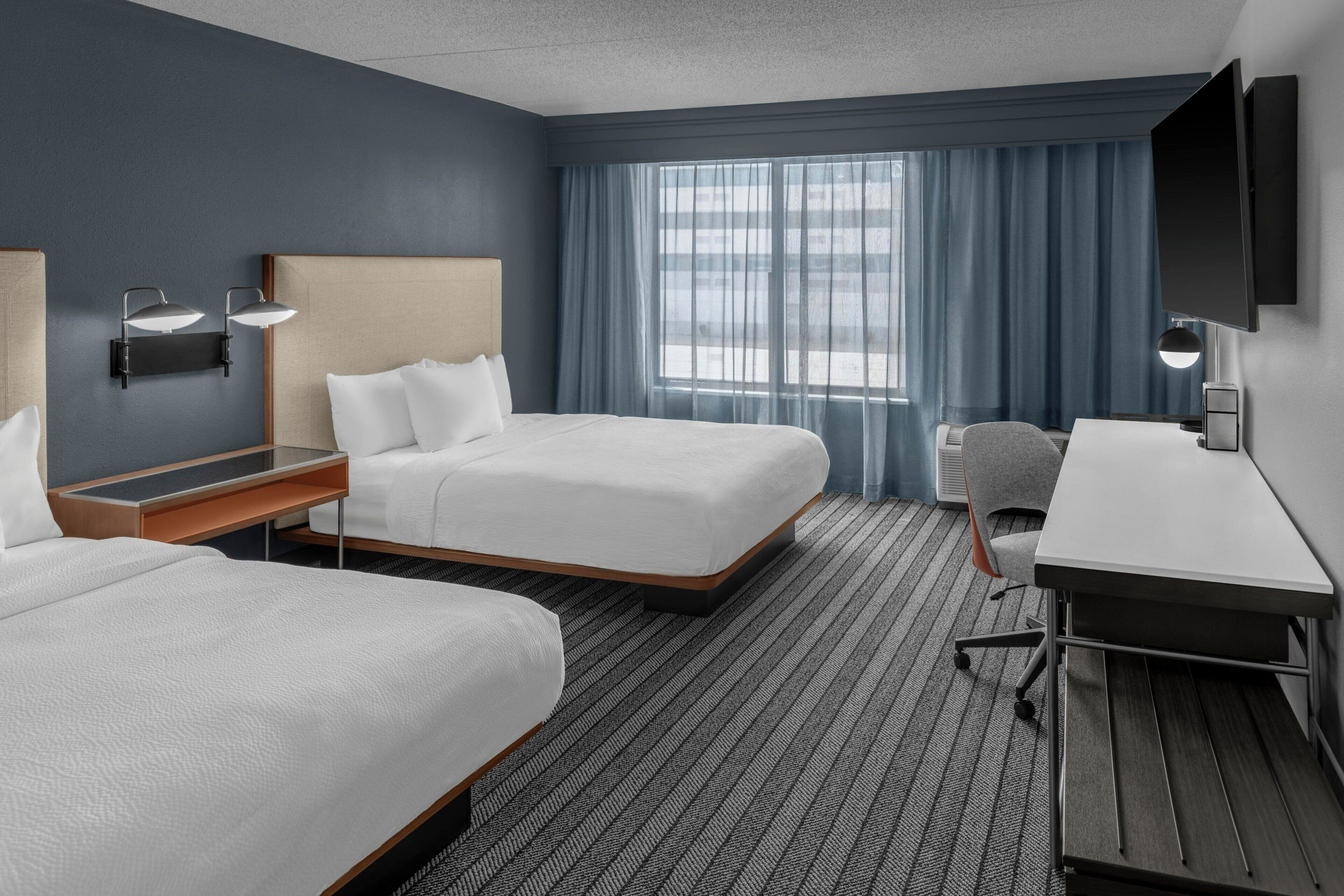 Une chambre d’hôtel avec deux lits, un bureau, une chaise, une télévision et une fenêtre avec des rideaux.