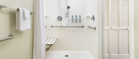 A bathroom with a walk-in shower, grab bars, a white bathtub, and a towel rack.