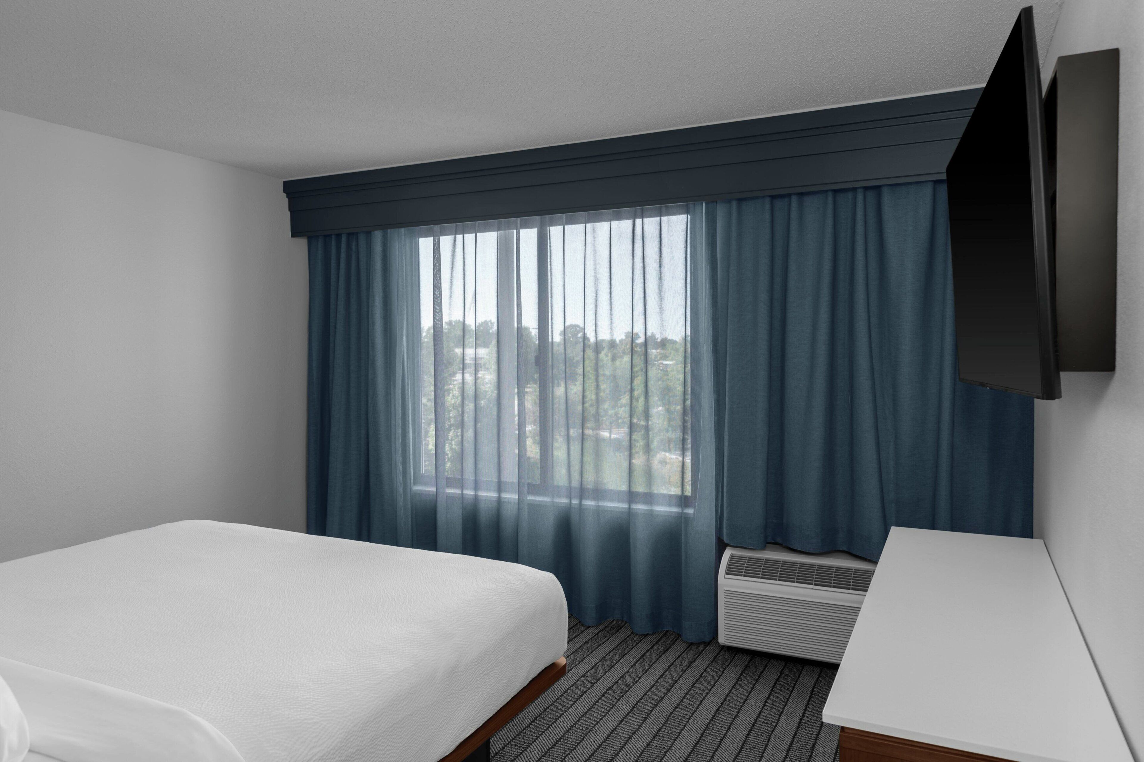 A hotel room with a bed, a desk, a flat-screen TV, and a window with curtains.