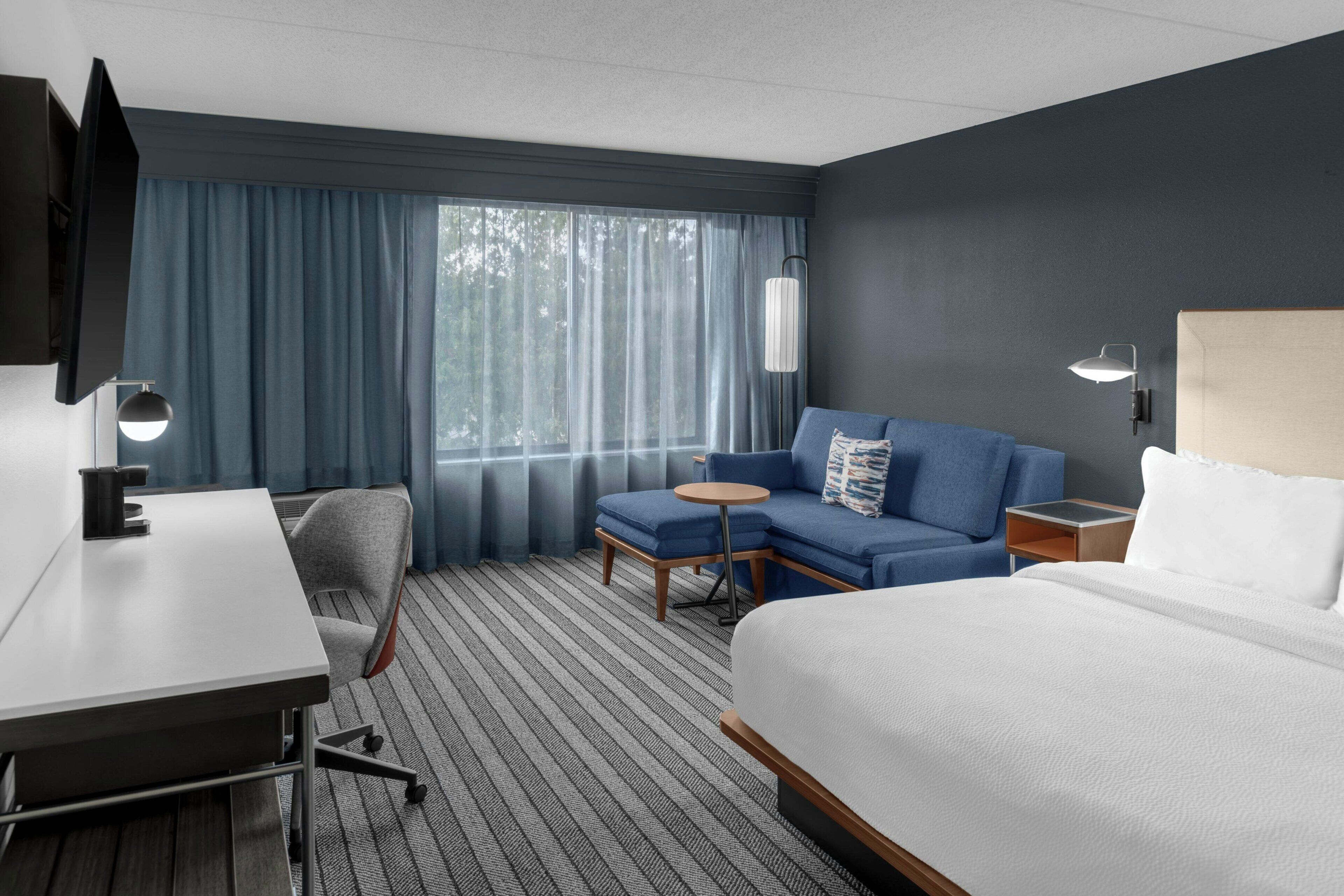 A hotel room with a bed, a desk, a chair, a sofa, a small table, and a TV.