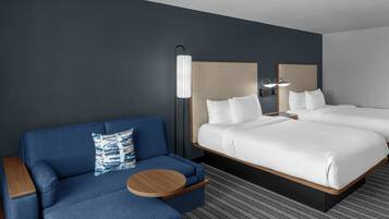 A hotel room with a bed, a blue sofa, a round wooden side table, and a patterned rug.