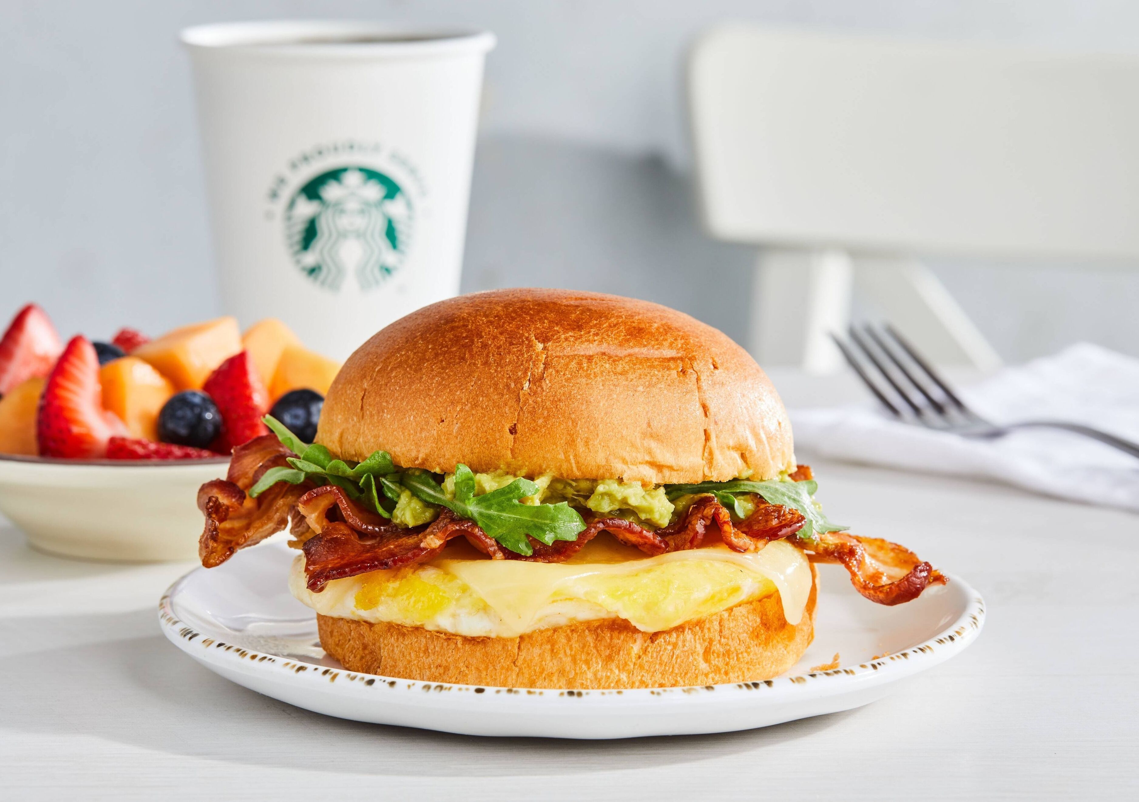 Un sándwich de desayuno en un plato, con una taza de Starbucks al fondo.