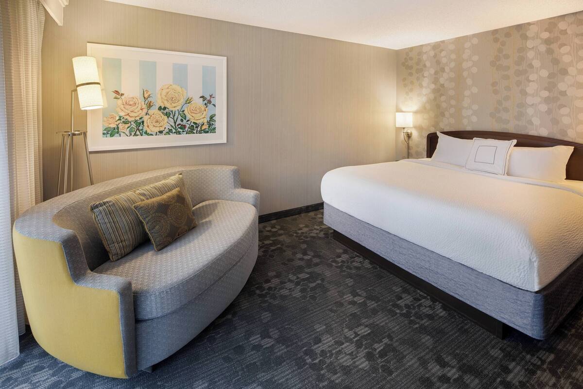 Una habitación de hotel con cama, sofá, un cuadro y dos lámparas.